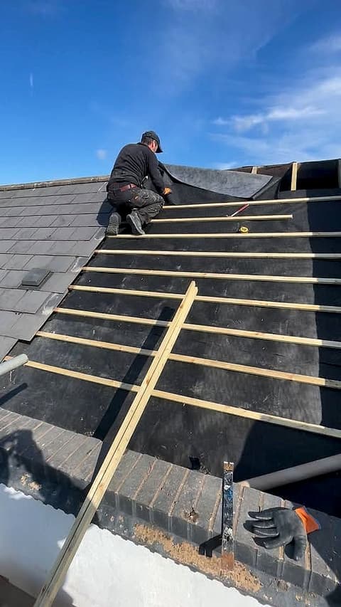 Roofer fixing new battens over membrane on a slate roof