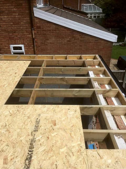 Timber roof joists and decking boards being laid on a single-storey extension